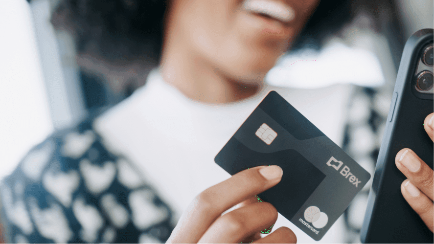 Close up of a woman smiling and holding a phone and Brex credit card